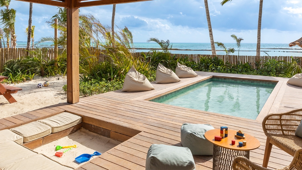 Beachfront wooden deck with pool, seating, and children's toys, overlooking the ocean.