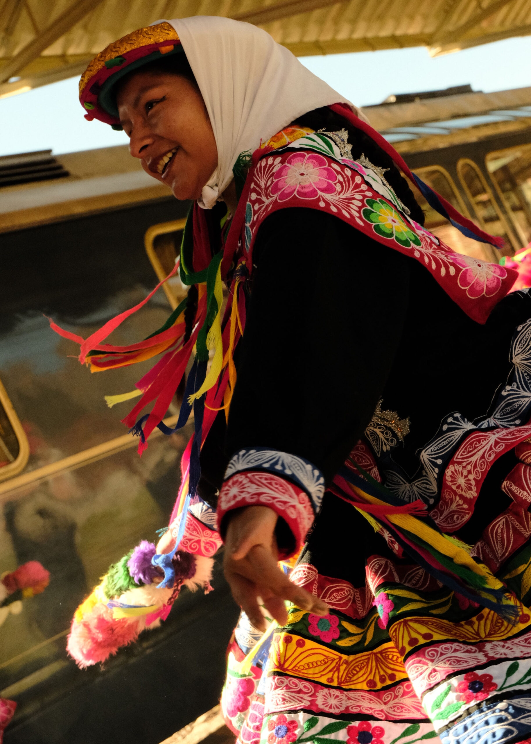 Person in vibrant traditional dress with colorful ribbons and headscarf.