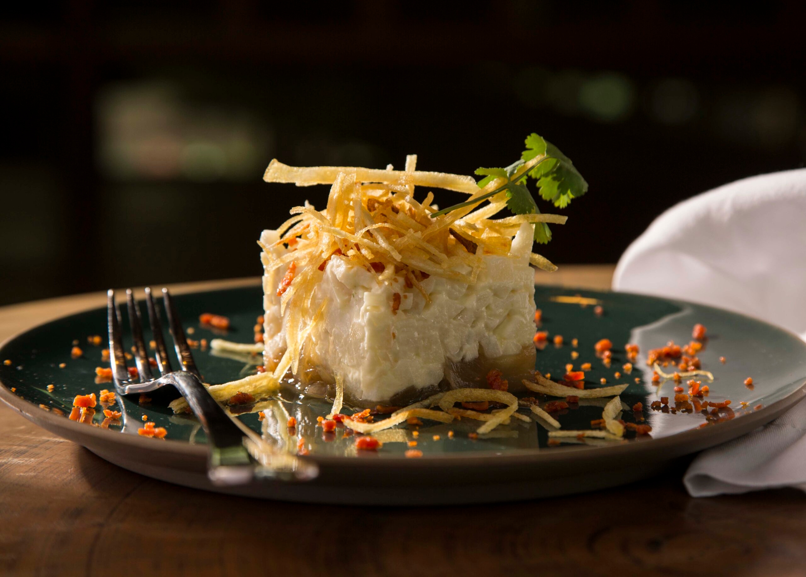 Gourmet dish with crispy potato topping on dark plate with fork.