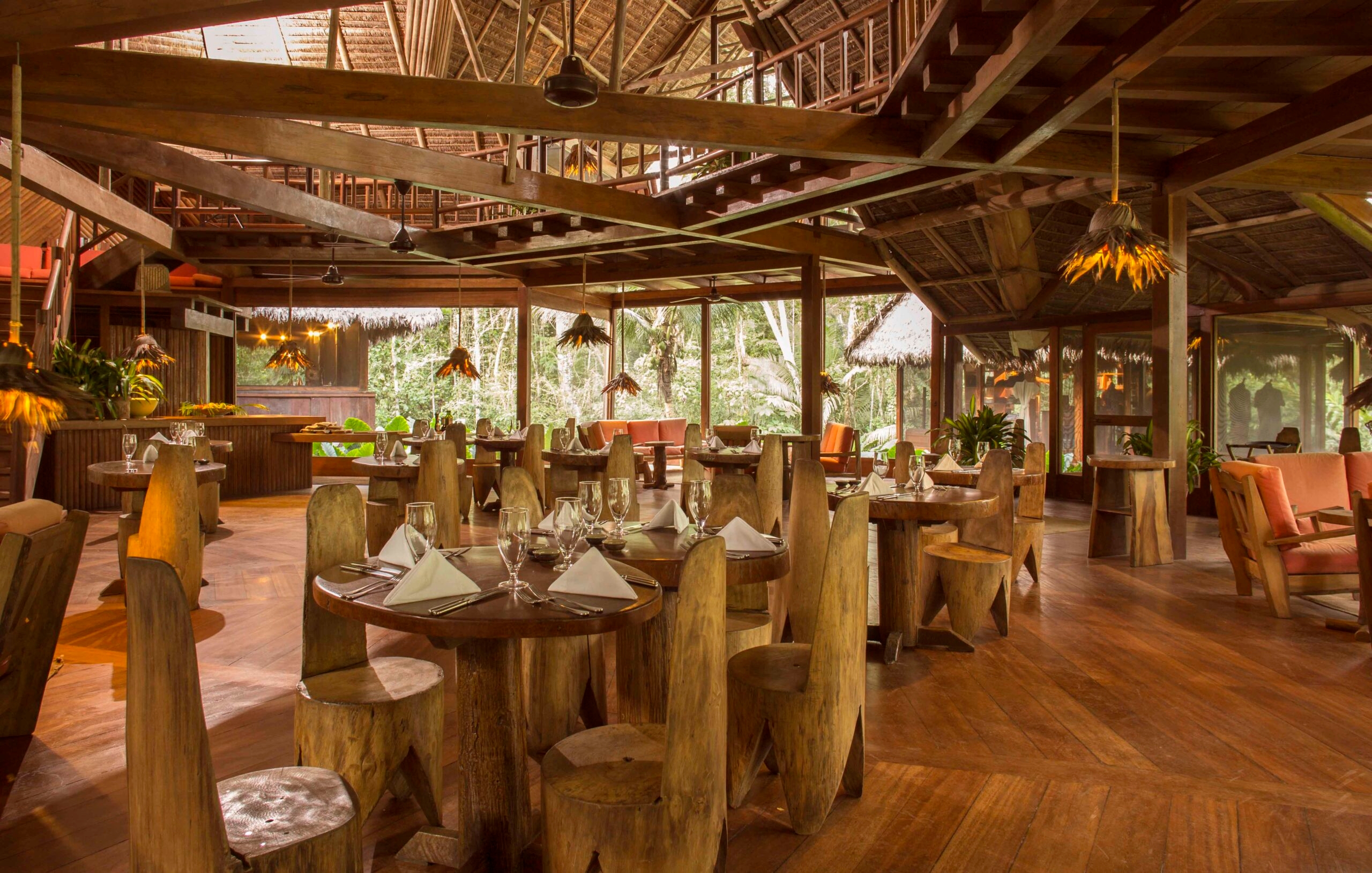 Rustic dining room with wooden furniture and tropical forest view through large windows.