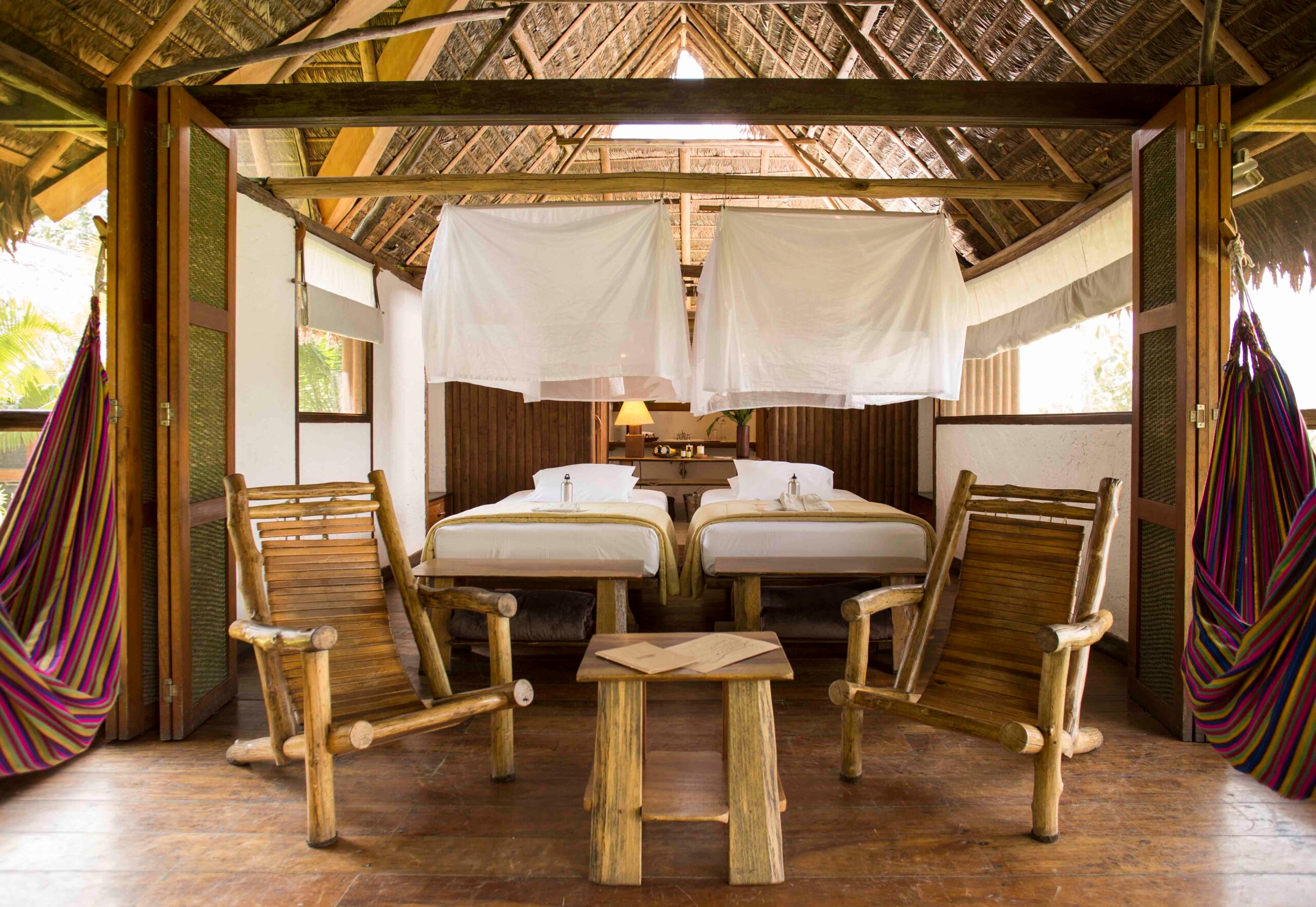 Rustic tropical bedroom with two beds, wooden furniture, and a striped hammock.