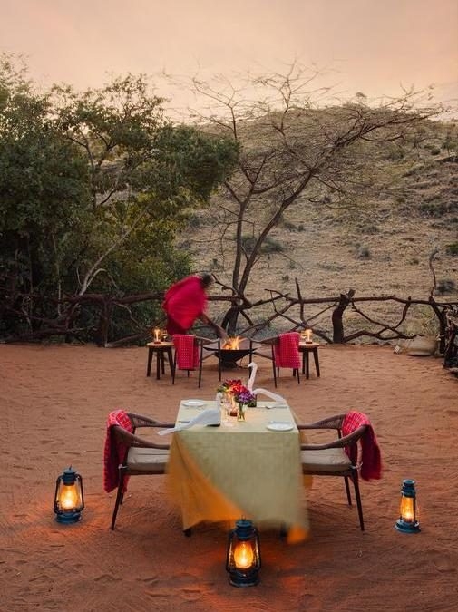 A private dining table set outdoors at dusk illuminated by lanterns and surrounded by nature.