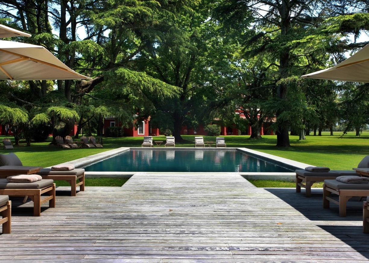 A serene poolside with loungers, umbrellas, and lush trees, flanked by a red building.