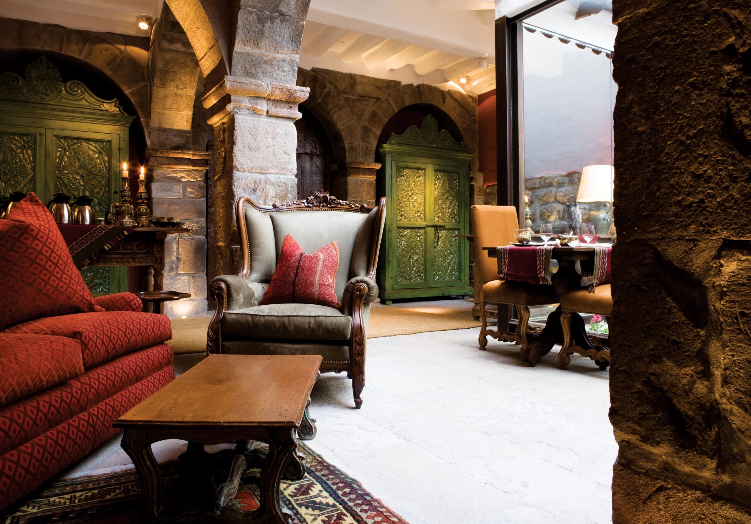 Elegant living room with red patterned sofa, armchair, and vintage furniture, adjacent to a cozy dining area.