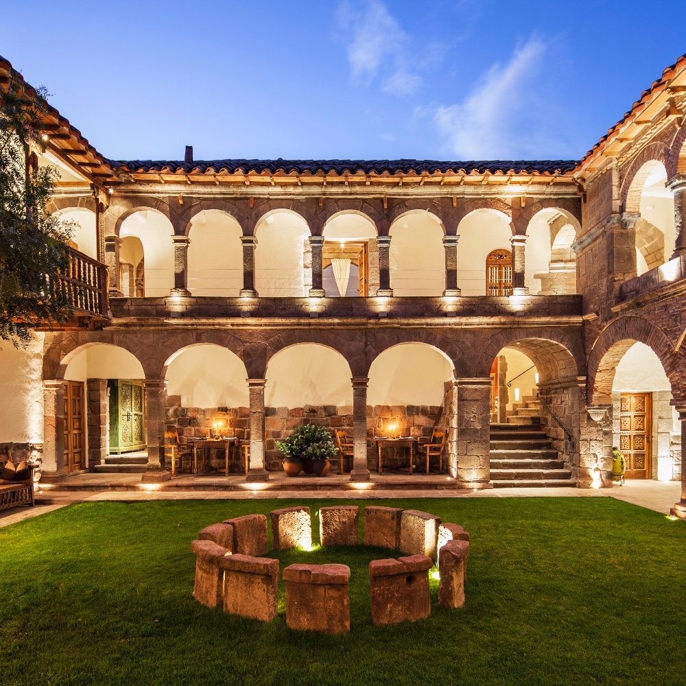 Elegant courtyard at twilight with arches, balcony, and lit interior rooms.