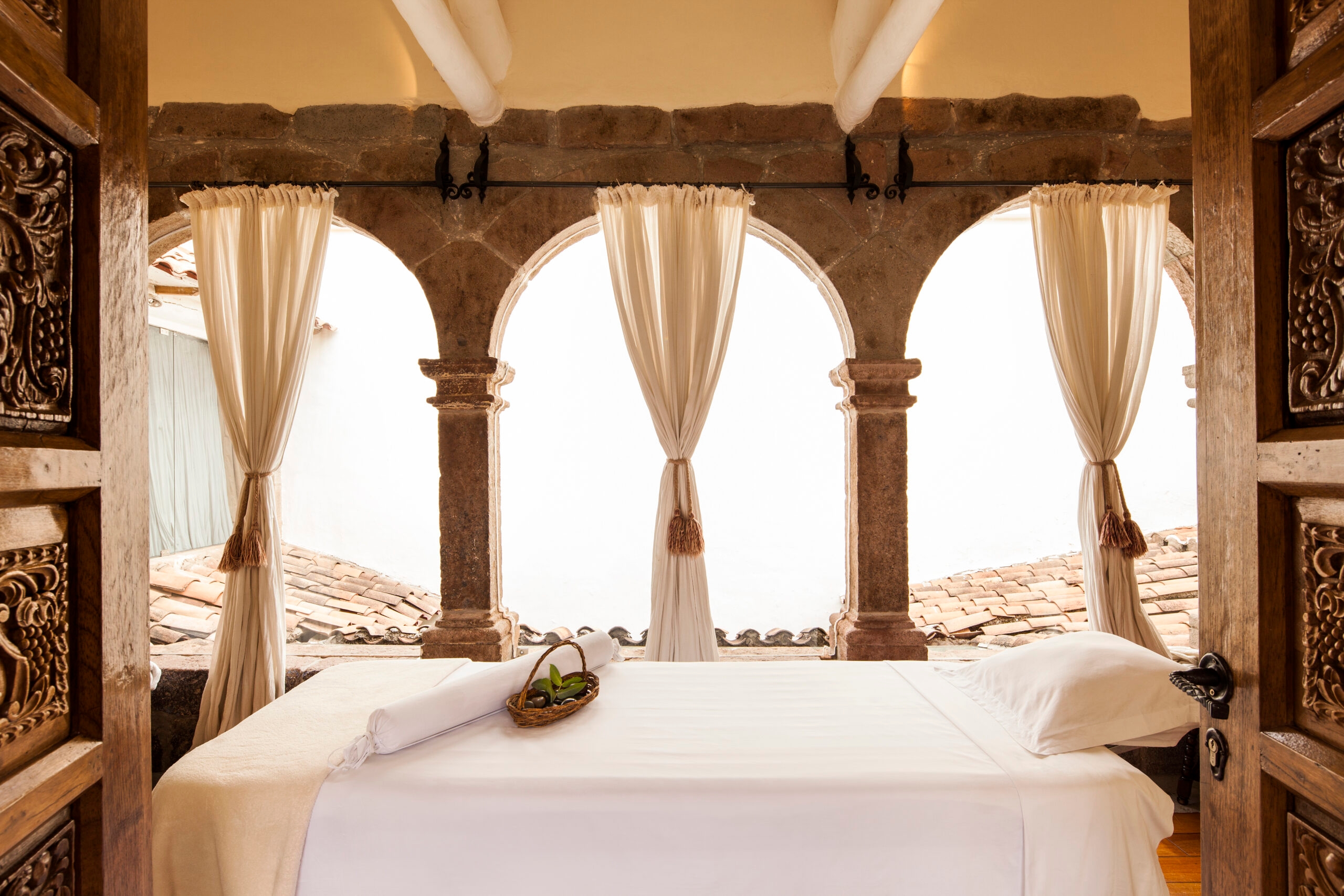 Rustic spa room with a massage table framed by arched stone doorways and draped curtains.