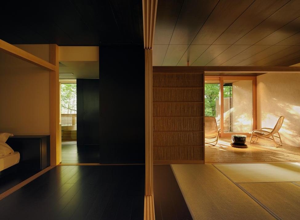 Minimalist Japanese suite with dark floors, tatami mats, and a bright terrace overlooking a garden.