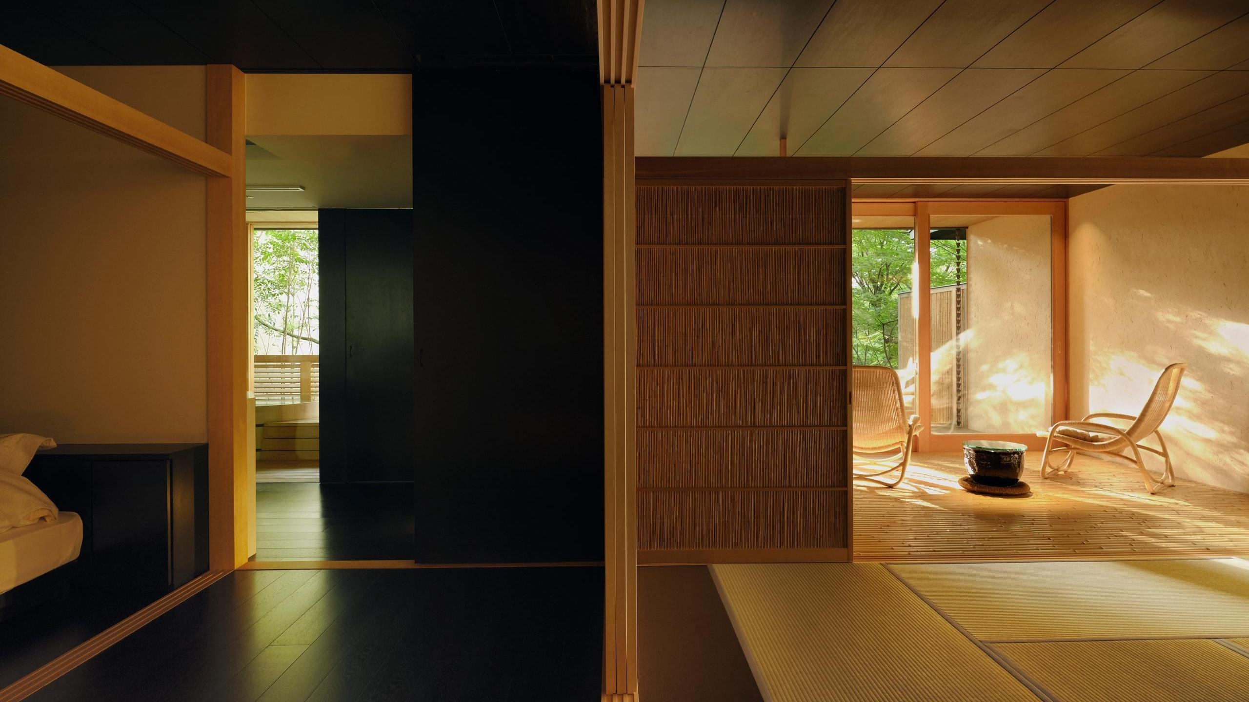 Minimalist Japanese suite with dark floors, tatami mats, and a bright terrace overlooking a garden.