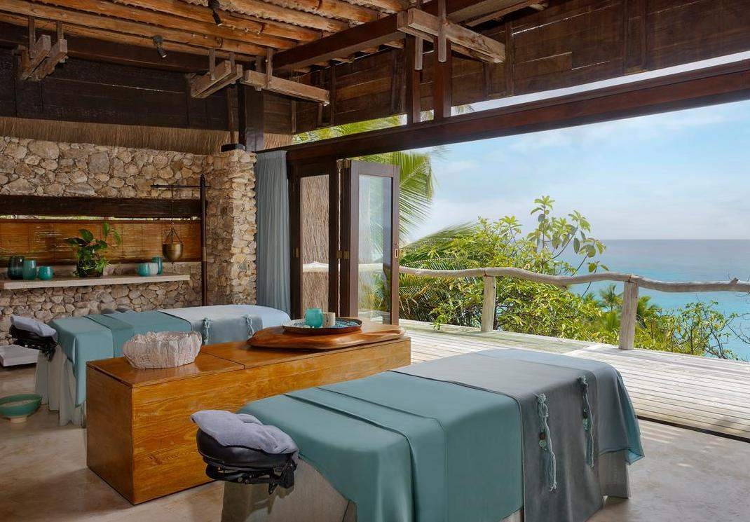 A tropical spa treatment room with massage tables overlooking the bright blue sea.