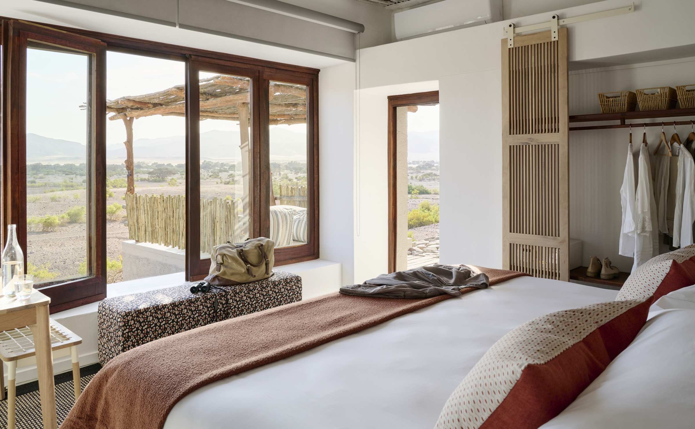 Bedroom with a king bed, open closet, and large glass doors leading out to a desert deck.