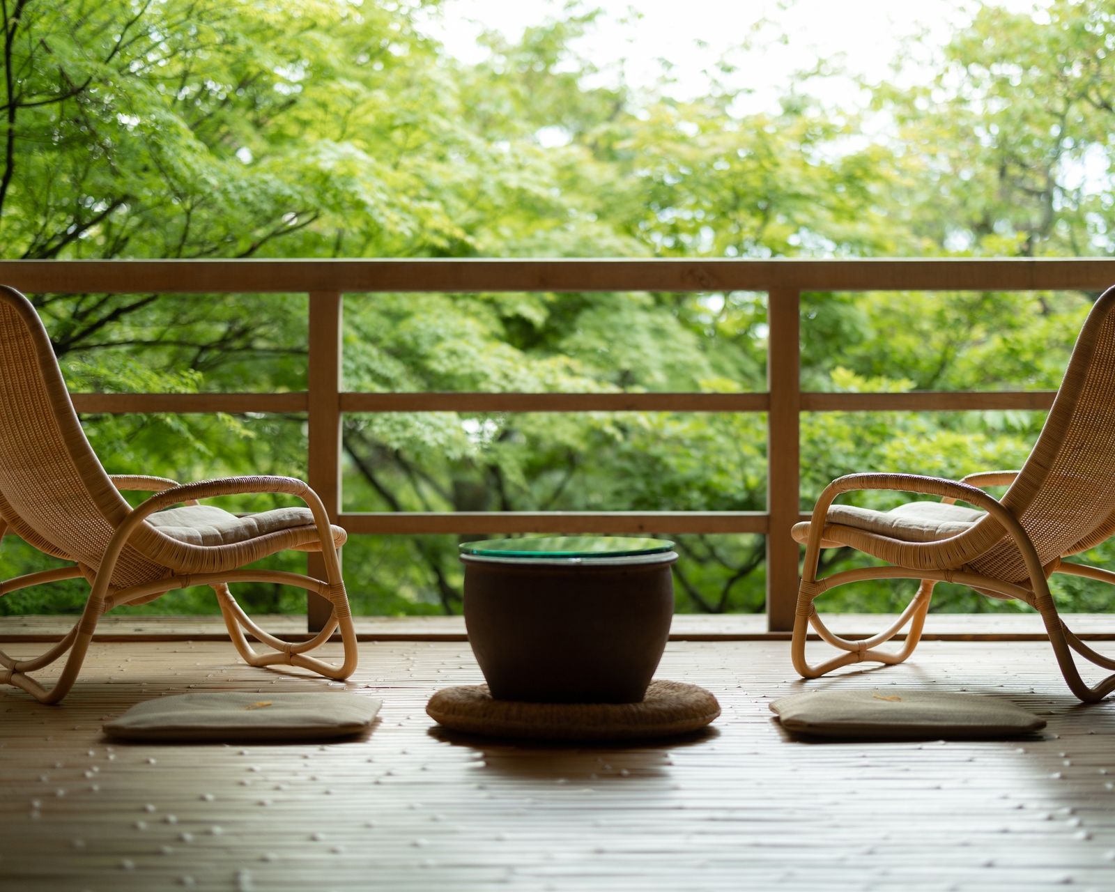 Two woven armchairs on a wooden terrace at Beniya Mukayu with an intimate view of a lush green forest.