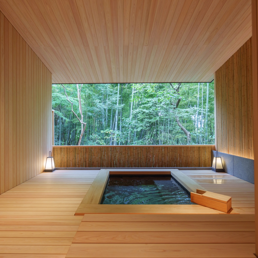 A wooden onsen bath at Beniya Mukayu in a peaceful room with a stunning view of a dense bamboo forest.