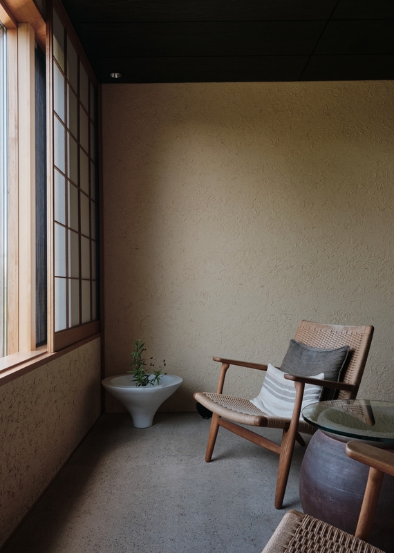 A minimalist Zen suite seating area with a wooden chair, a side table, and a white plant bowl by a paper screen window.