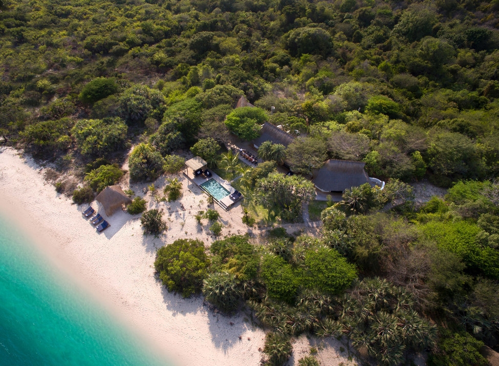 Aerial view of a private pool, thatched buildings, and white sandy beach at andBeyond Benguerra Island.