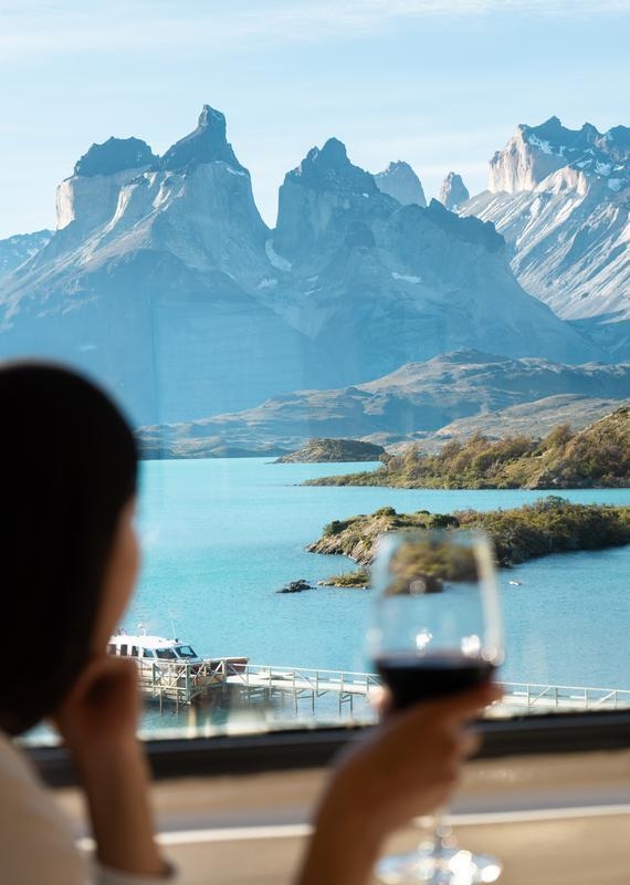 Silhouette of a person holding a wine glass while looking through an Explora Patagonia window at sharp mountains.