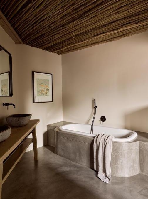 A modern luxury bathroom with a bathtub, wooden vanity, stone sinks, and a stick ceiling.