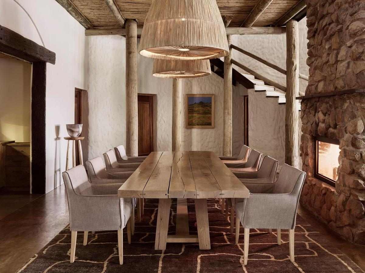 A spacious indoor dining room with a wooden table, stone fireplace, and woven pendant lamps.