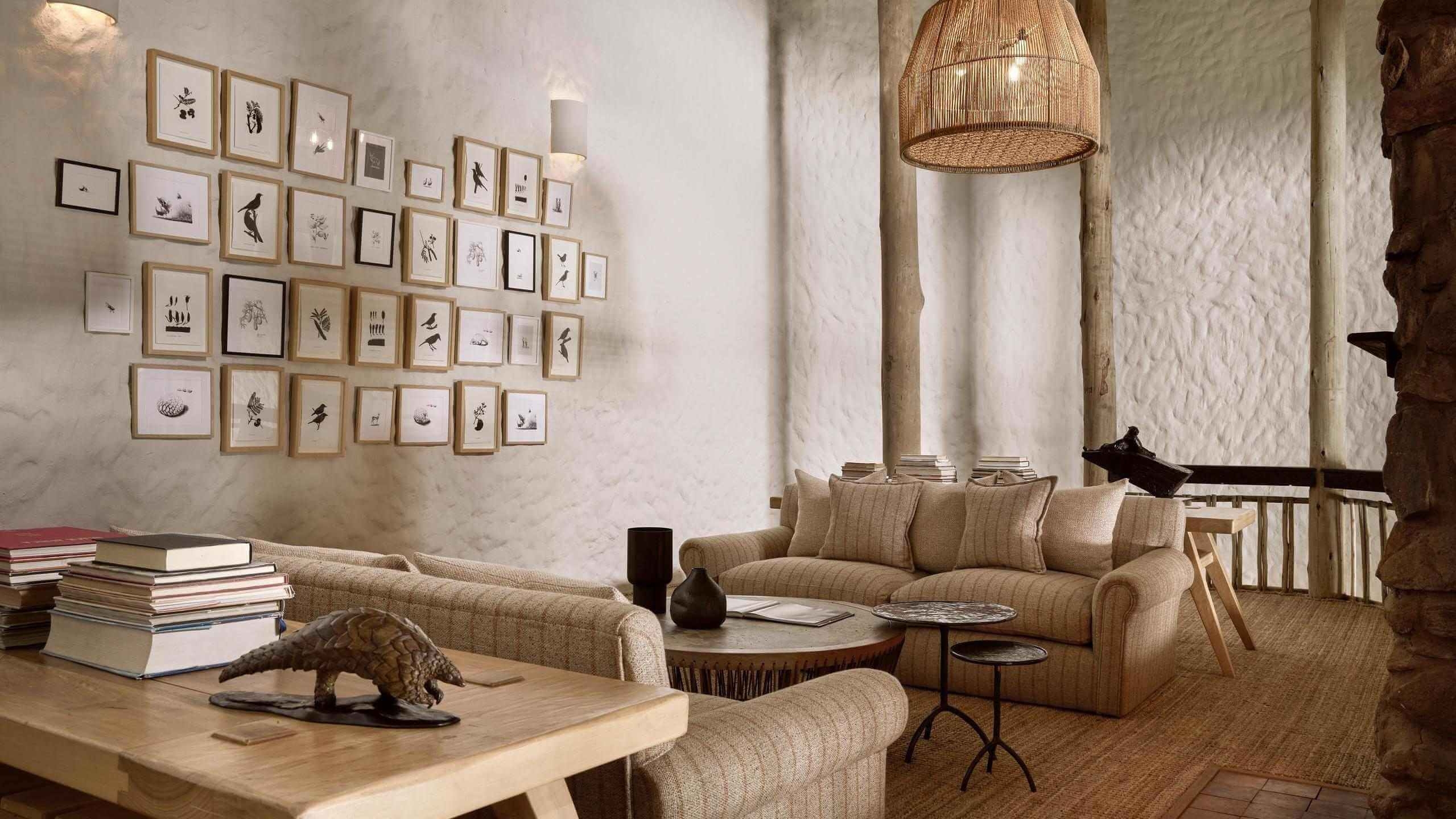 A mezzanine lounge area with beige sofas, stacks of books, a framed picture gallery wall, and a woven pendant light.