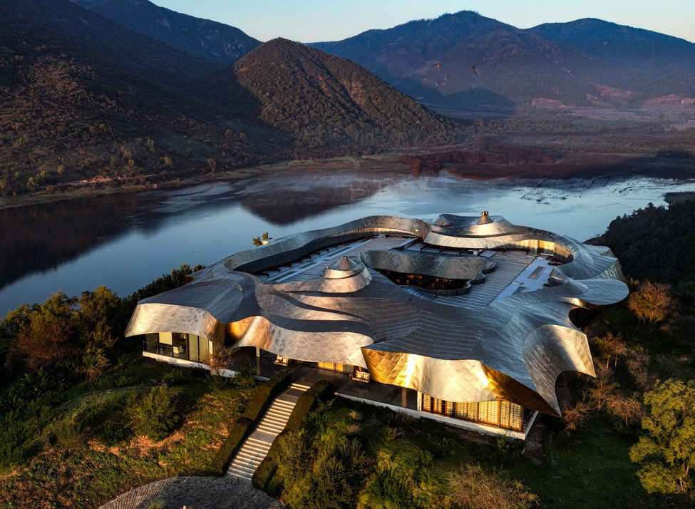 Aerial view of Vik Chile showing a modern building with a flowing silver metal roof overlooking a lake and mountains.