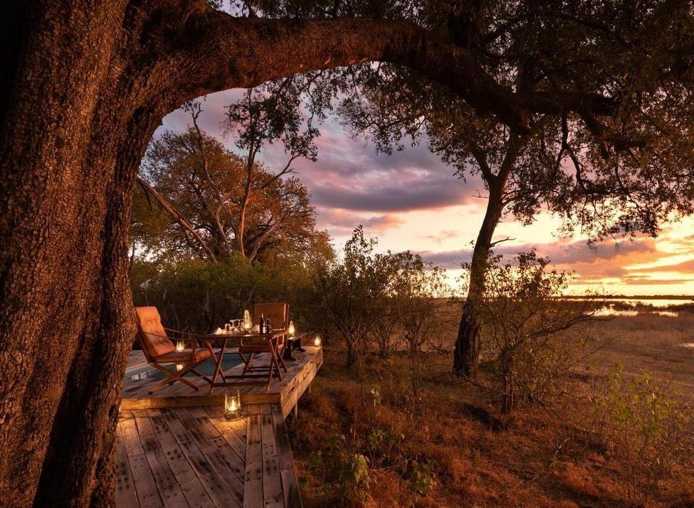 Candlelit dinner table for two on a wooden deck at Zarafa Camp, Botswana, overlooking the savanna at sunset.