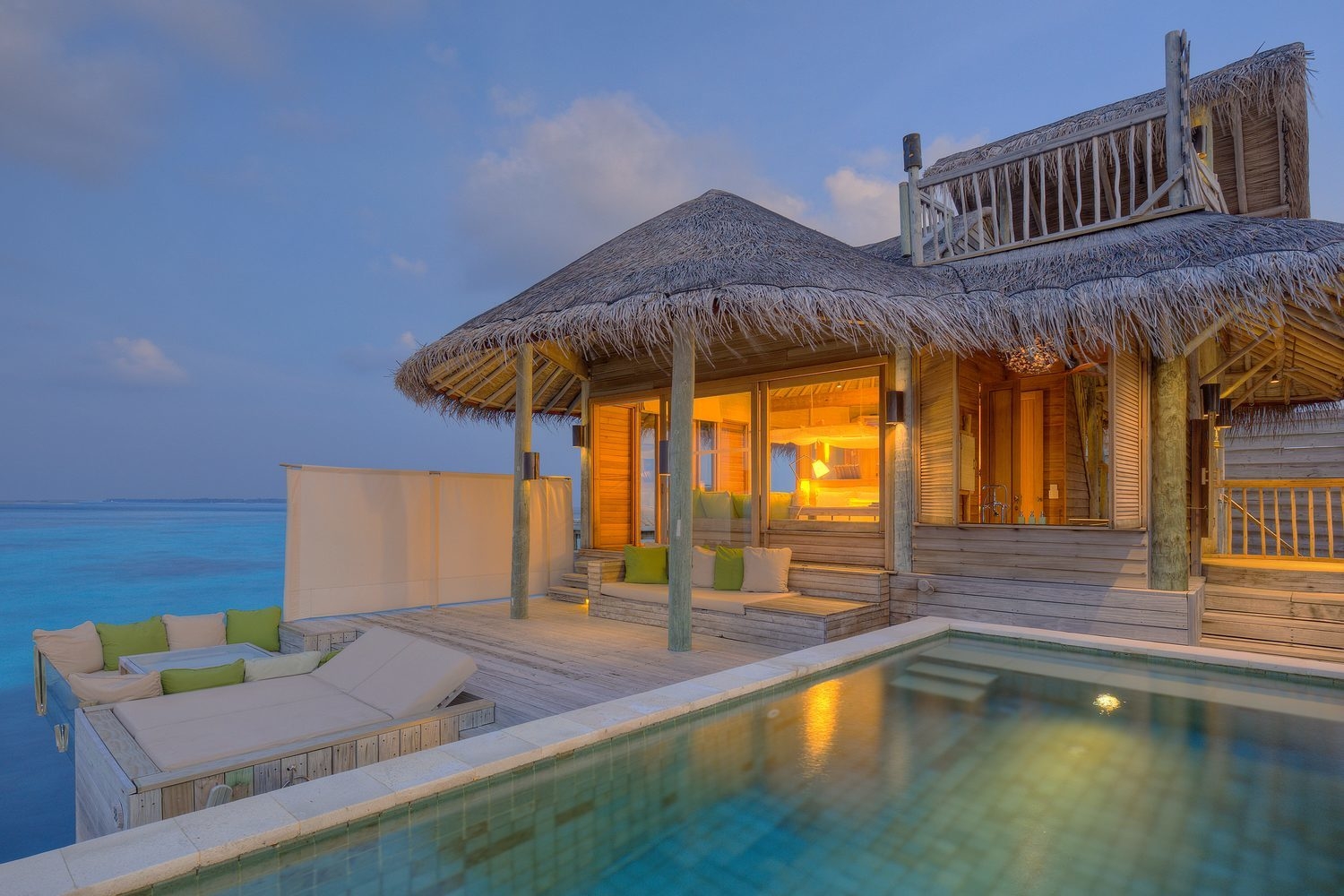 Overwater villa lit up at dusk at Six Senses Laamu