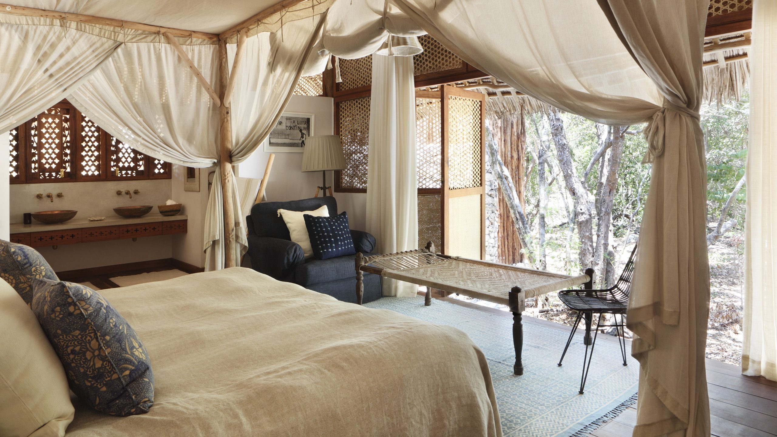 A serene bedroom featuring a draped bed, stylish furniture, and open windows overlooking a lush natural landscape.