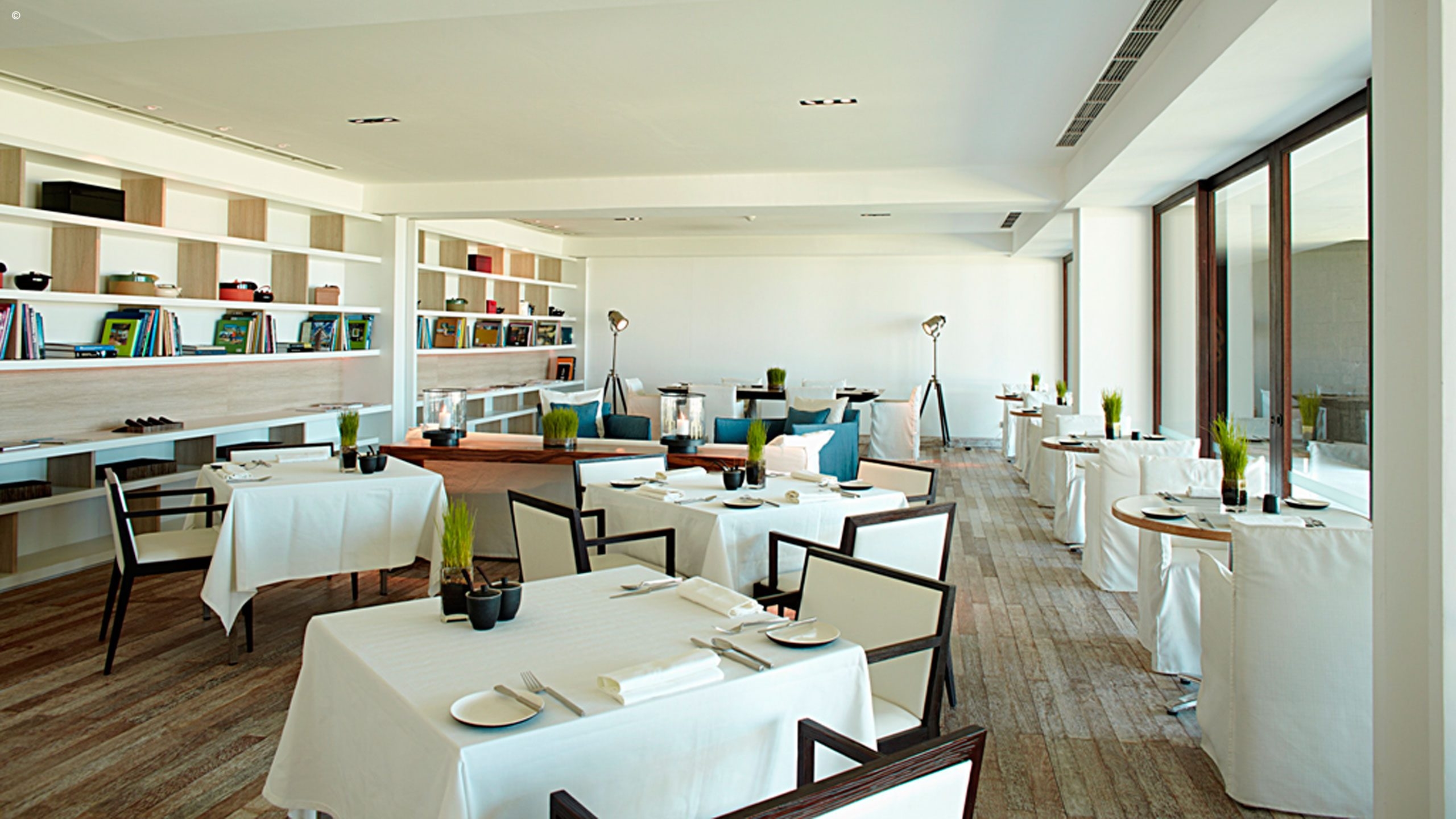 Modern restaurant interior featuring neatly arranged tables, minimalist decor, and large windows, creating a bright, airy atmosphere.