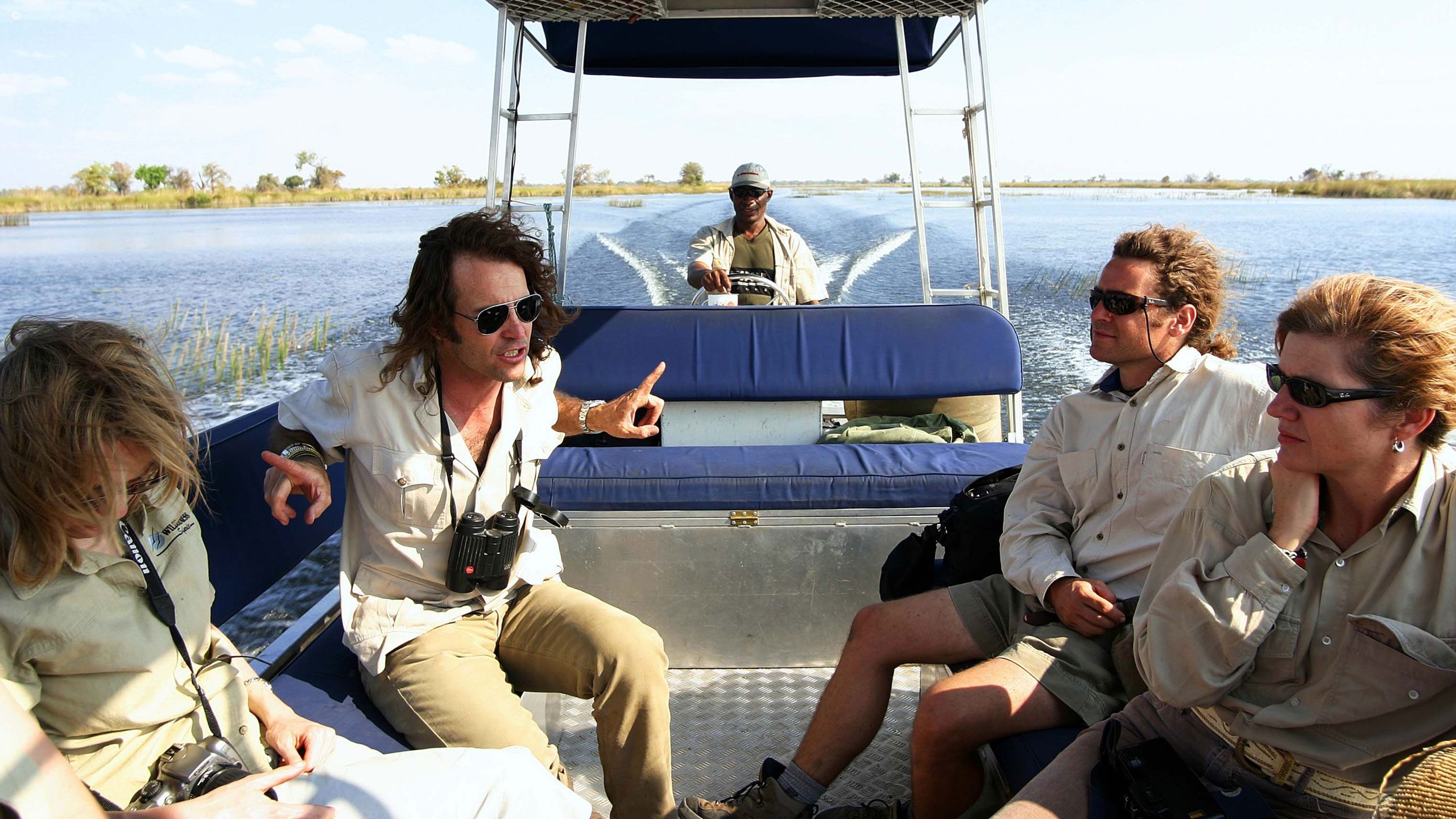 A guide driving a motor-powered boat through a delta with four passengers sitting in front in mid-conversation
