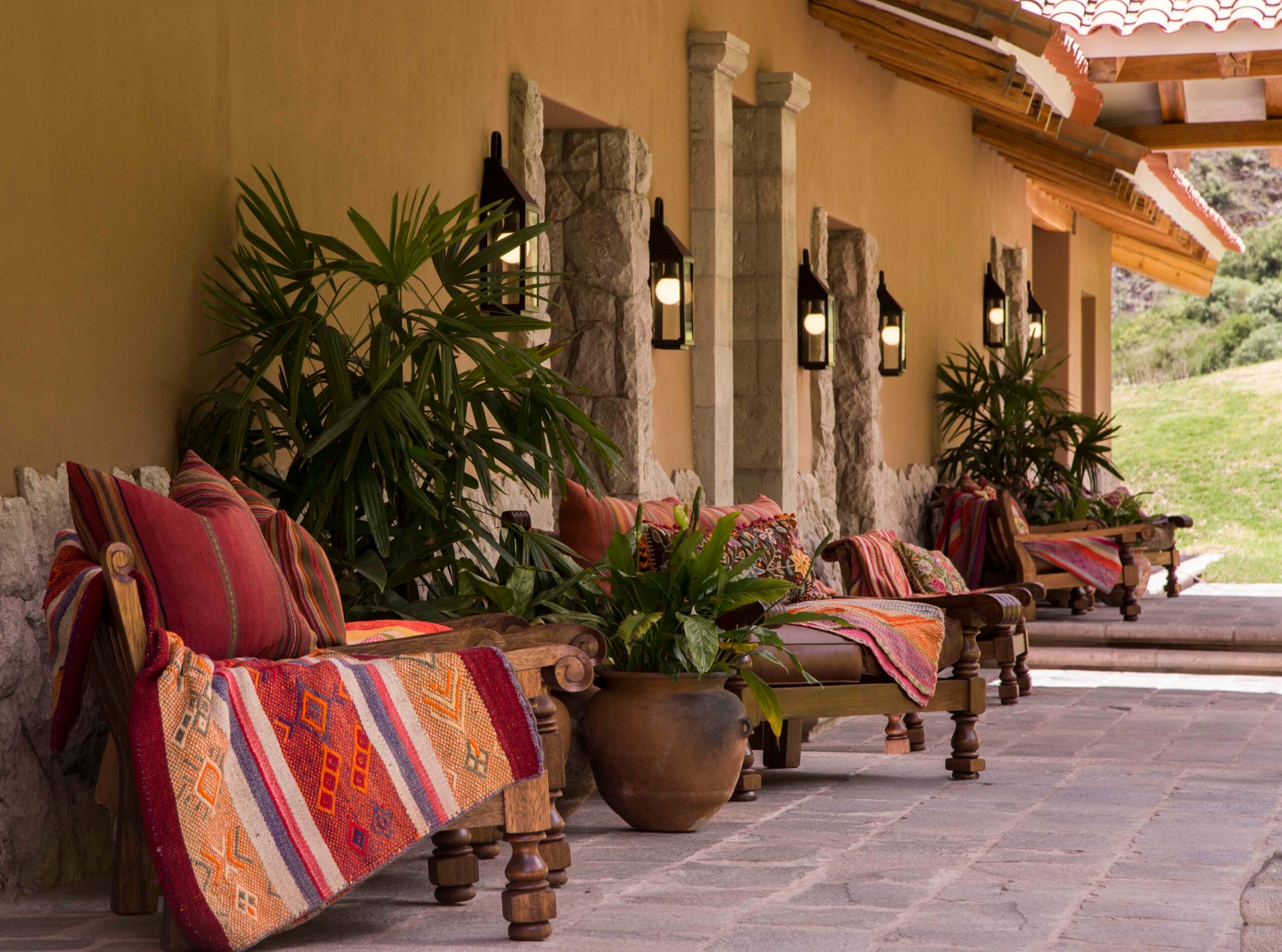 Rustic outdoor seating area with wooden benches adorned with colorful textiles and plants.