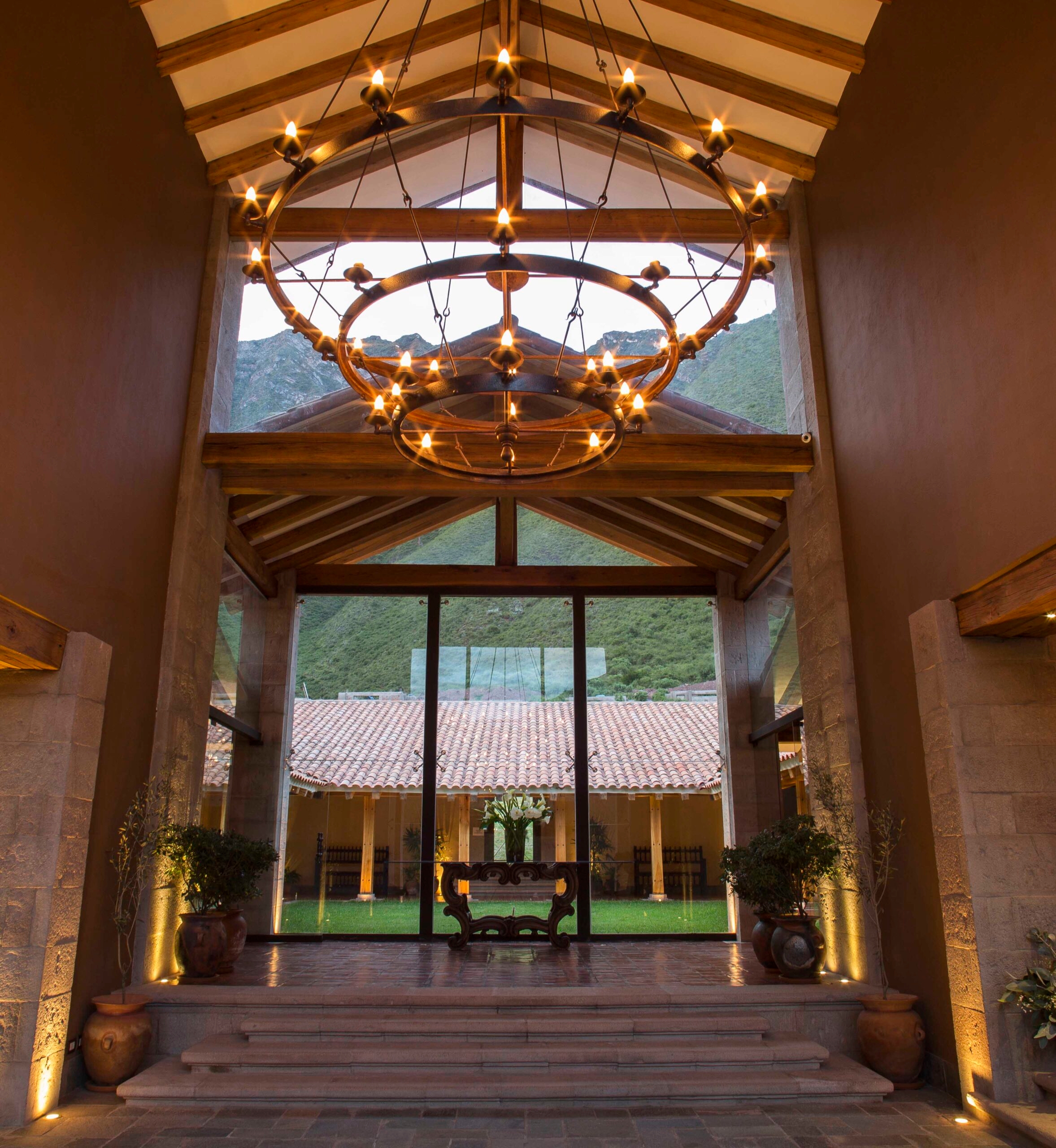 Elegant indoor space with a circular chandelier, overlooking a courtyard and mountains.