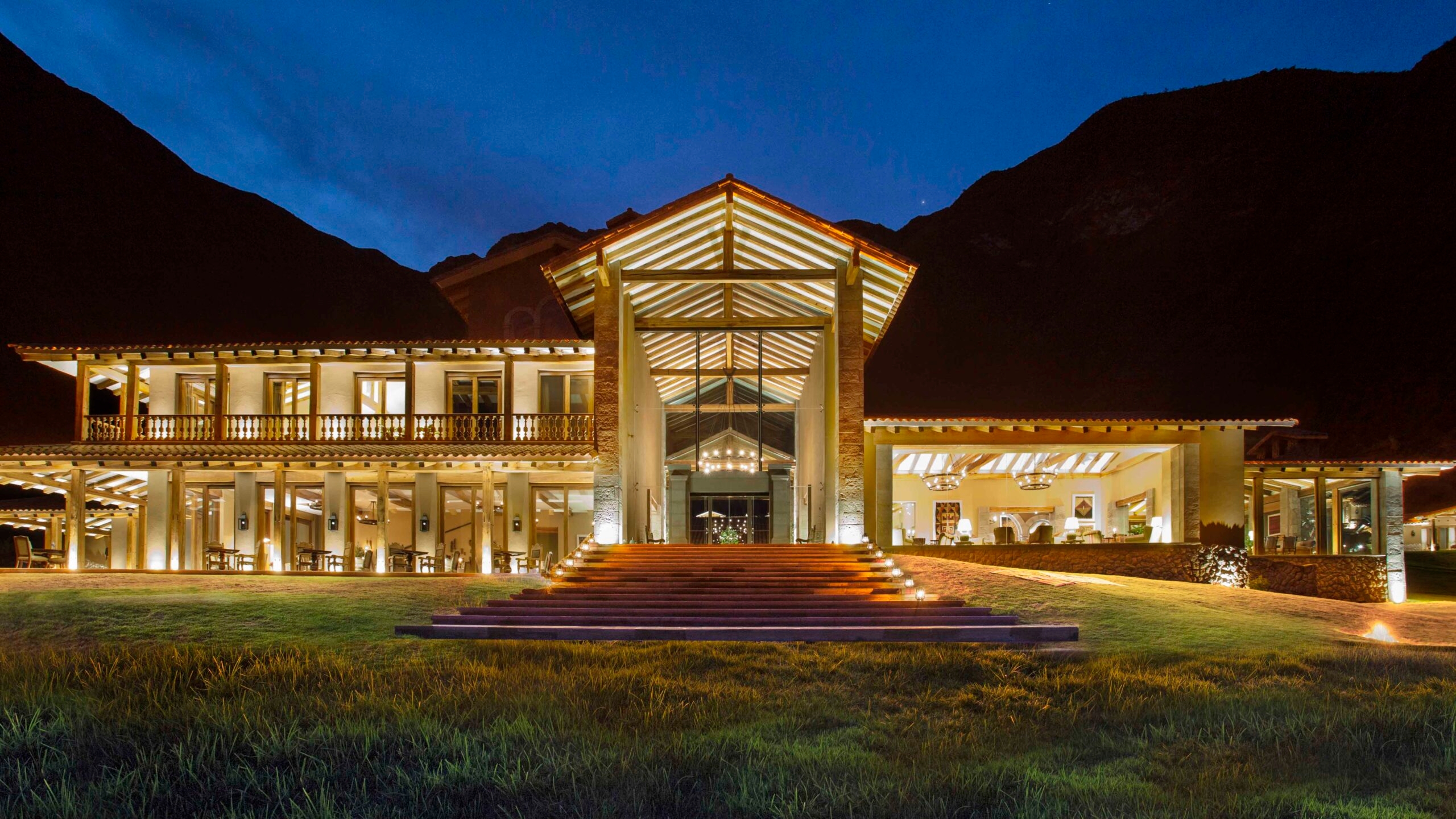 Illuminated two-story building at dusk with large front steps and mountain backdrop.