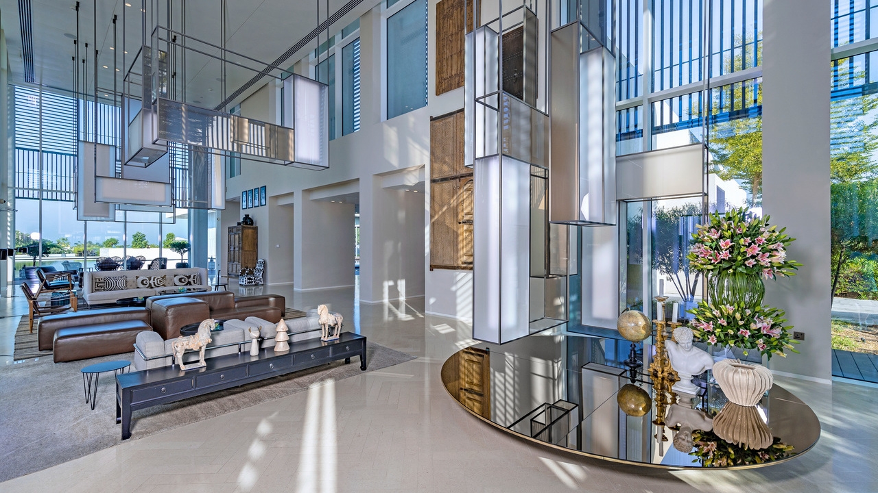 Large modern hotel lobby with tall glass walls, brown leather seating, and unique rectangular hanging lanterns.