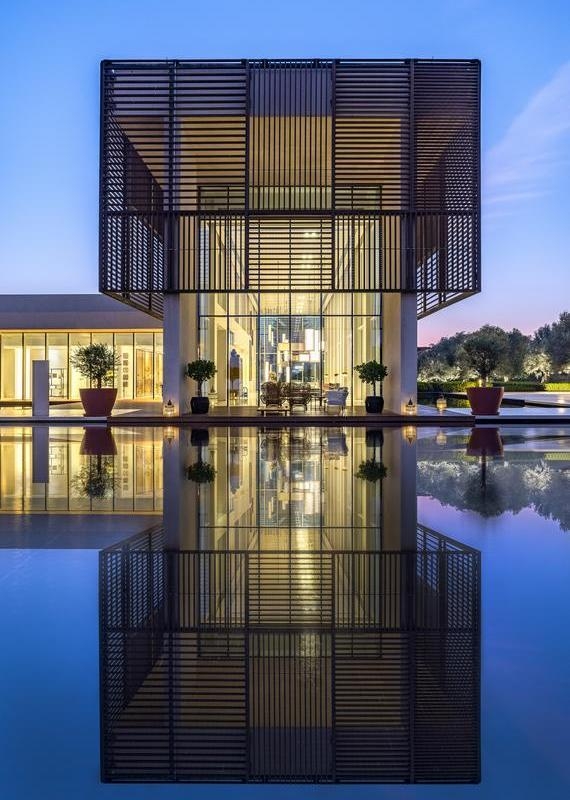 Modern building facade with horizontal slats reflecting in a large still pool during blue hour at Al Zorah Beach Resort.