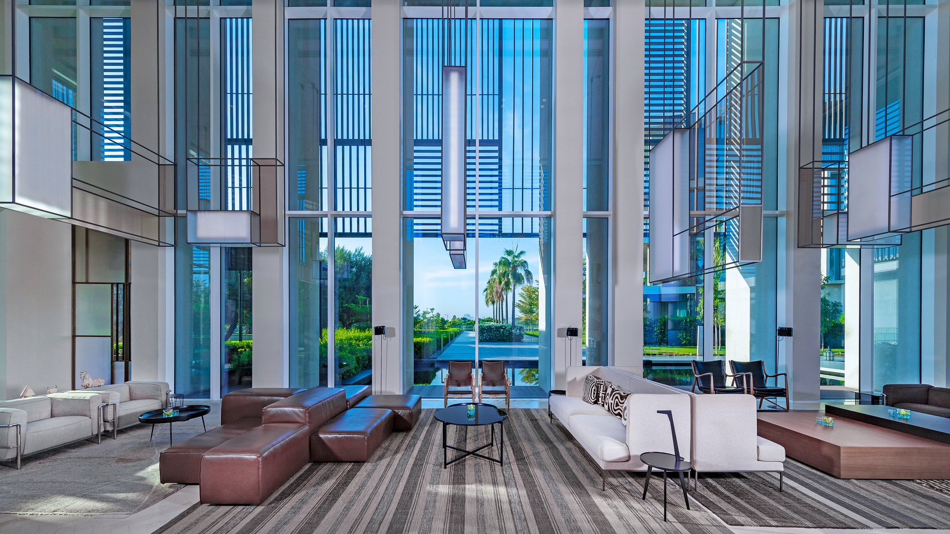 Spacious resort lobby with tall light installations, a mirrored table with flowers, and stylish lounge furniture.