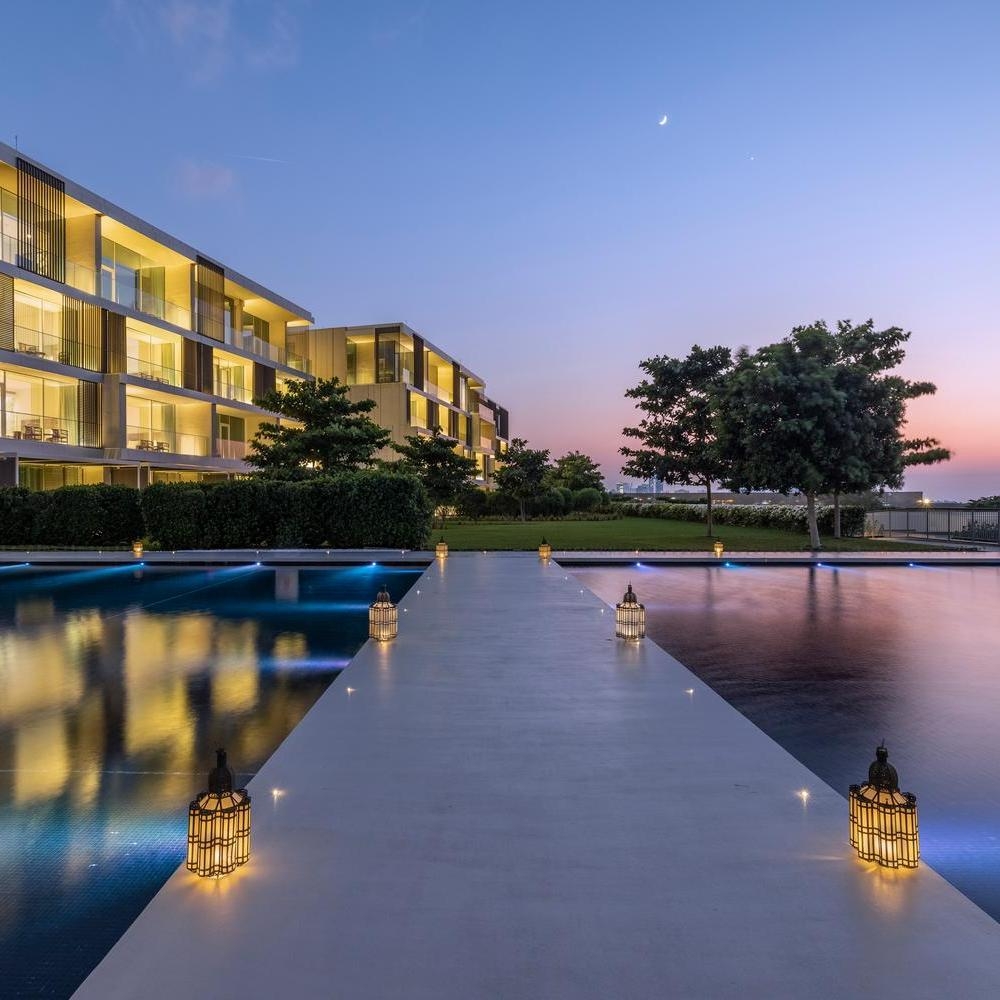 Night view of a modern multi-story building and a concrete path over water lit by traditional lanterns.