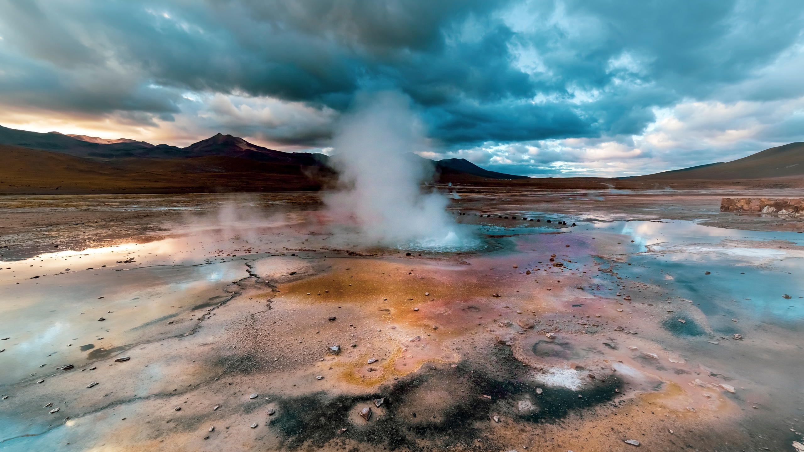 Steam rises from a geothermal spring in a barren landscape at dusk.