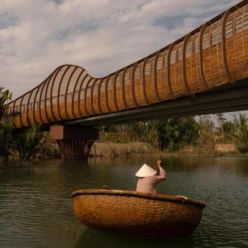 A person in a traditional basket boat paddling under a bamboo bridge at Namia River Retreat.