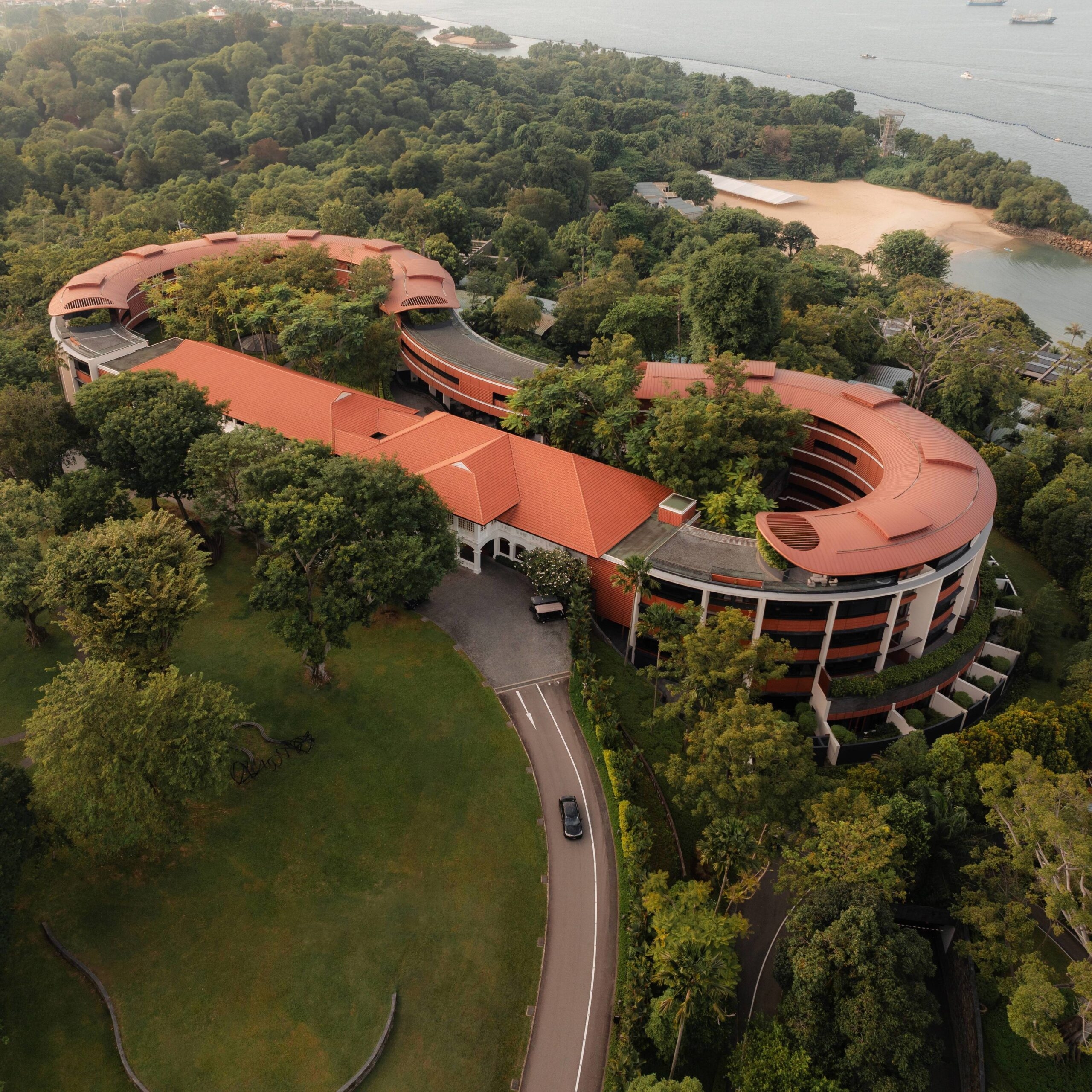 Aerial view of circular terracotta-roofed buildings nestled in greenery near water.