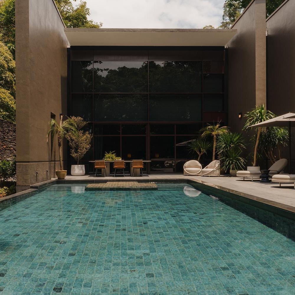 Modern home exterior with a large pool, patio furniture, and floor-to-ceiling windows.