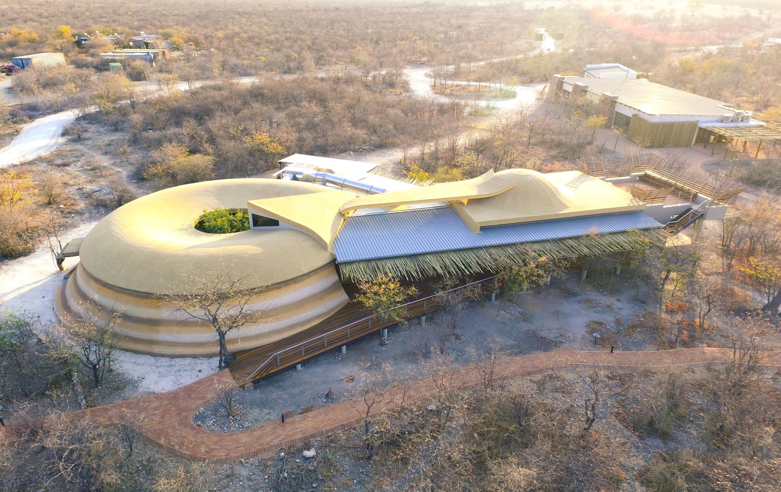 Aerial view of a unique circular building with a green roof in a dry landscape.