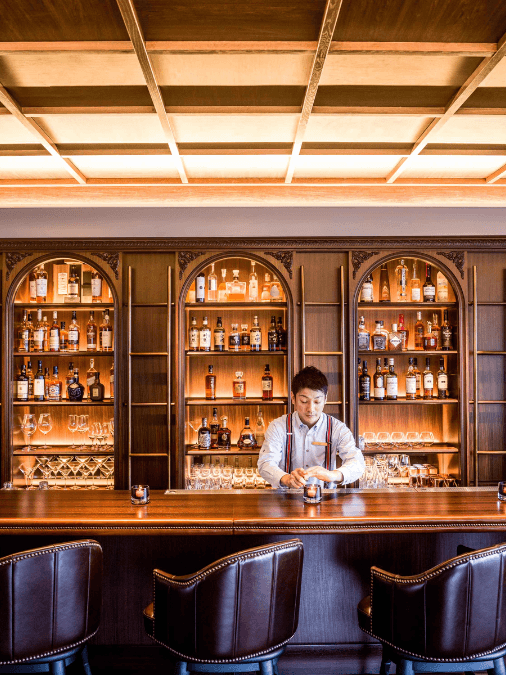A bartender standing in front of brightly illuminated shelves of bottles