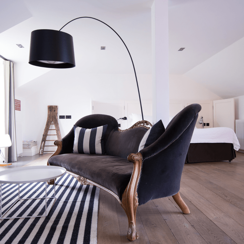 Modern hotel room with a black velvet sofa, floor lamp and black-and-white striped rug