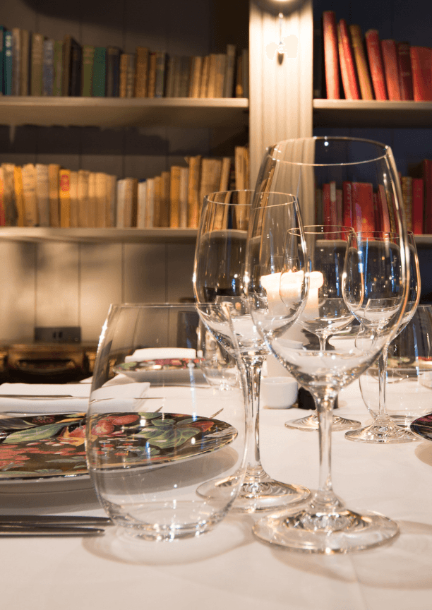 Close-up of wine glasses and water glasses on a candlelit table with a bookshelf in the background