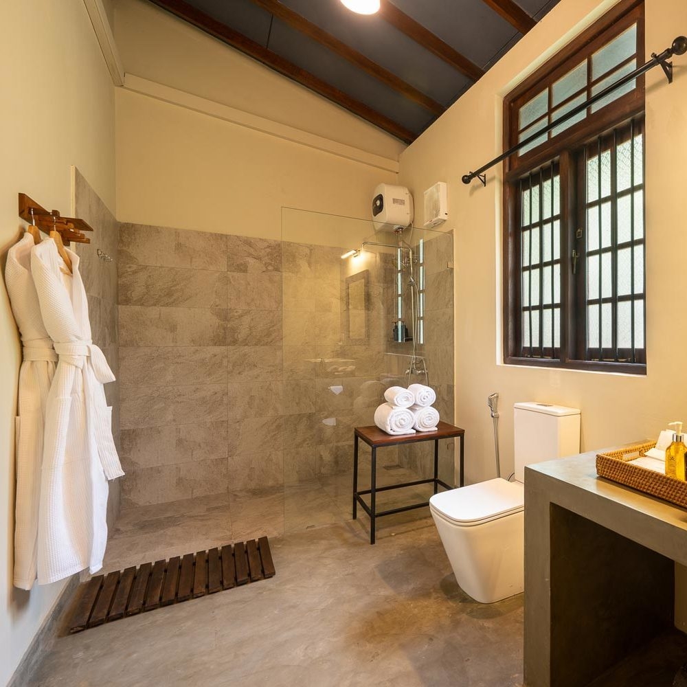 Modern bathroom featuring a glass shower, white toilet, and wooden accents with white robes hanging.