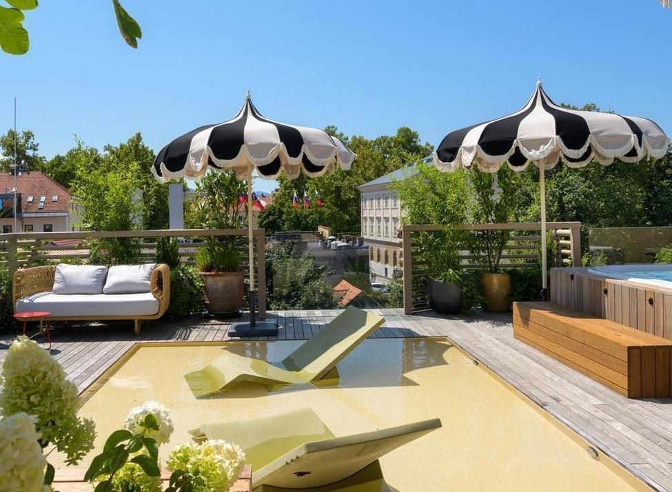 Rooftop terrace at AS Boutique Hotel with lounge chairs in a shallow pool under black and white striped umbrellas.