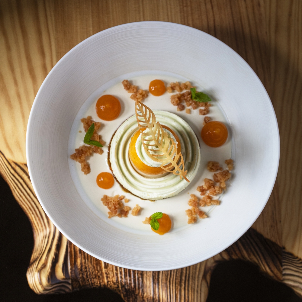 Overhead shot of a carefully plated meal with dollops and swirls on a white plate placed on a wood table.