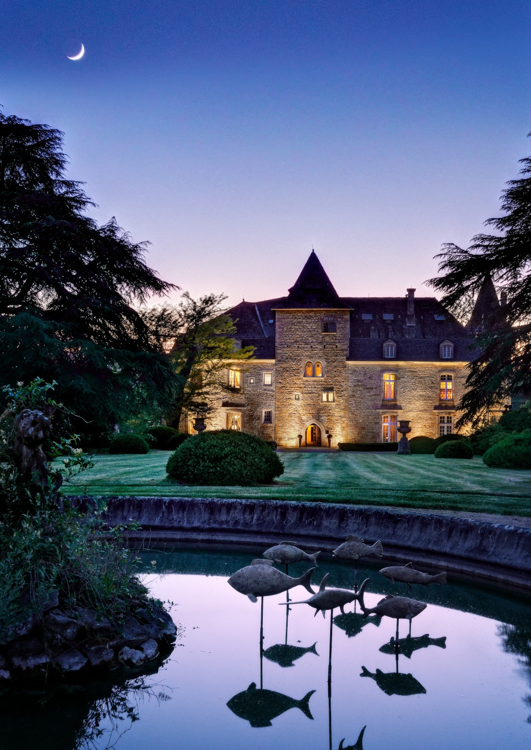 Exterior evening shot of the castle uplit with a pond and lawn in the foreground and purple sunset sky.