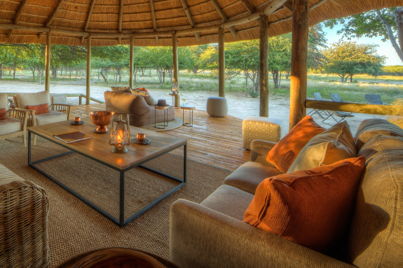 An indoor-outdoor lounge area with sofas and lanterns under a thatched roof at Dinaka Botswana property.