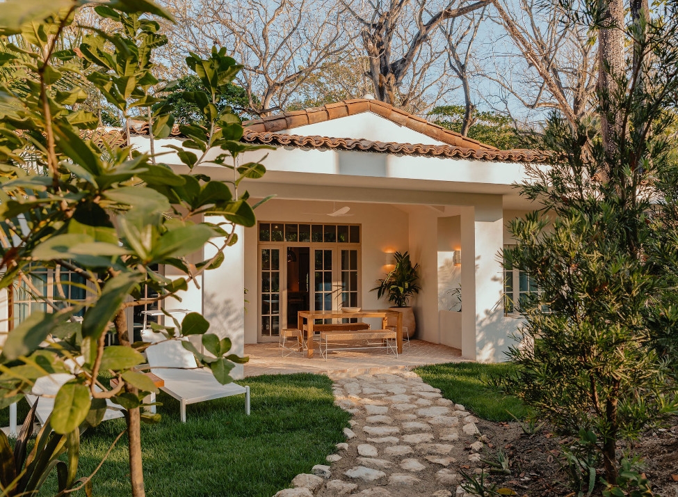 Exterior of a white villa entrance with a stone pathway leading up to it and a picnic table out the front.