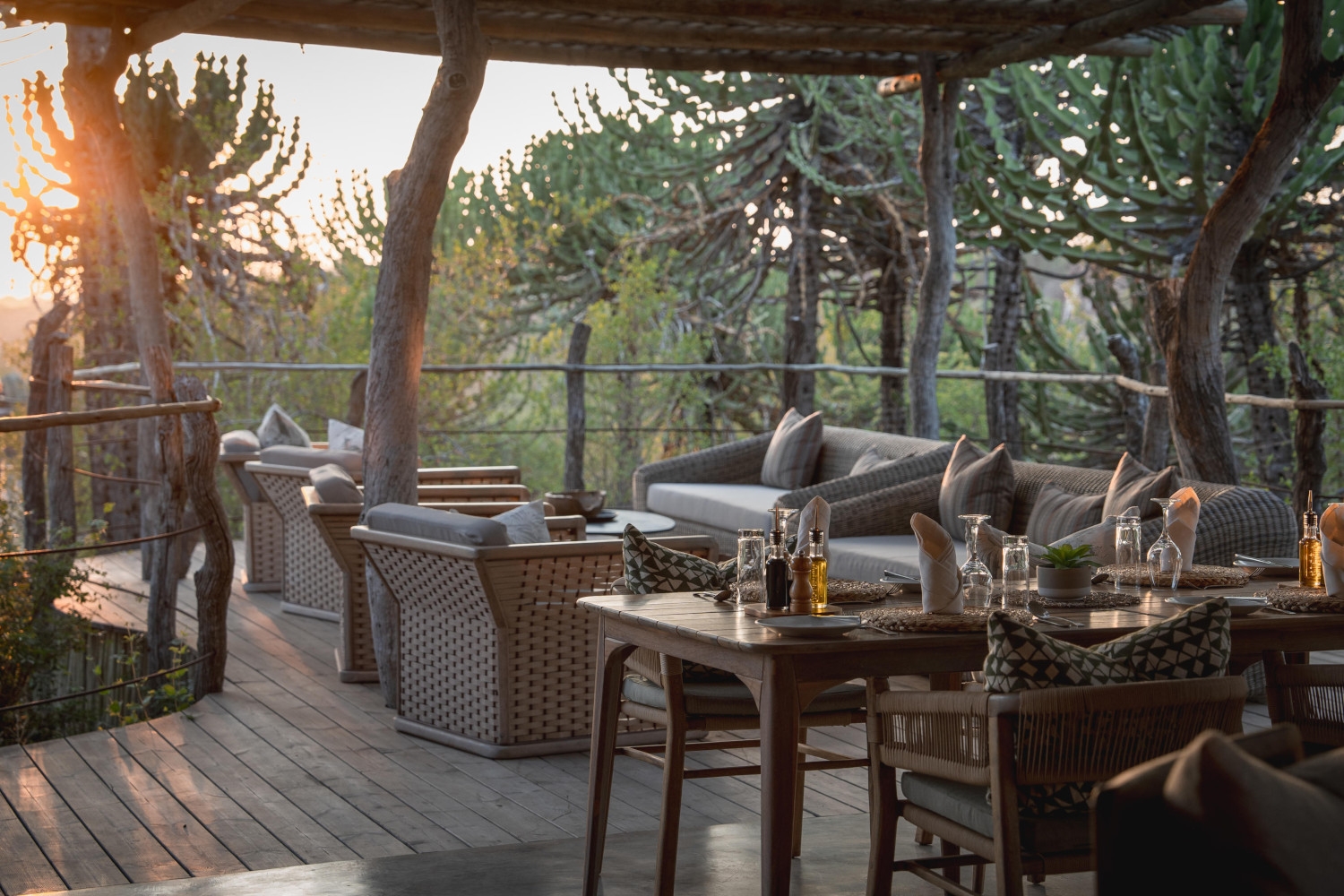 Covered wooden terrace deck with various lounge chairs and tables surrounded by succulent trees and plants.